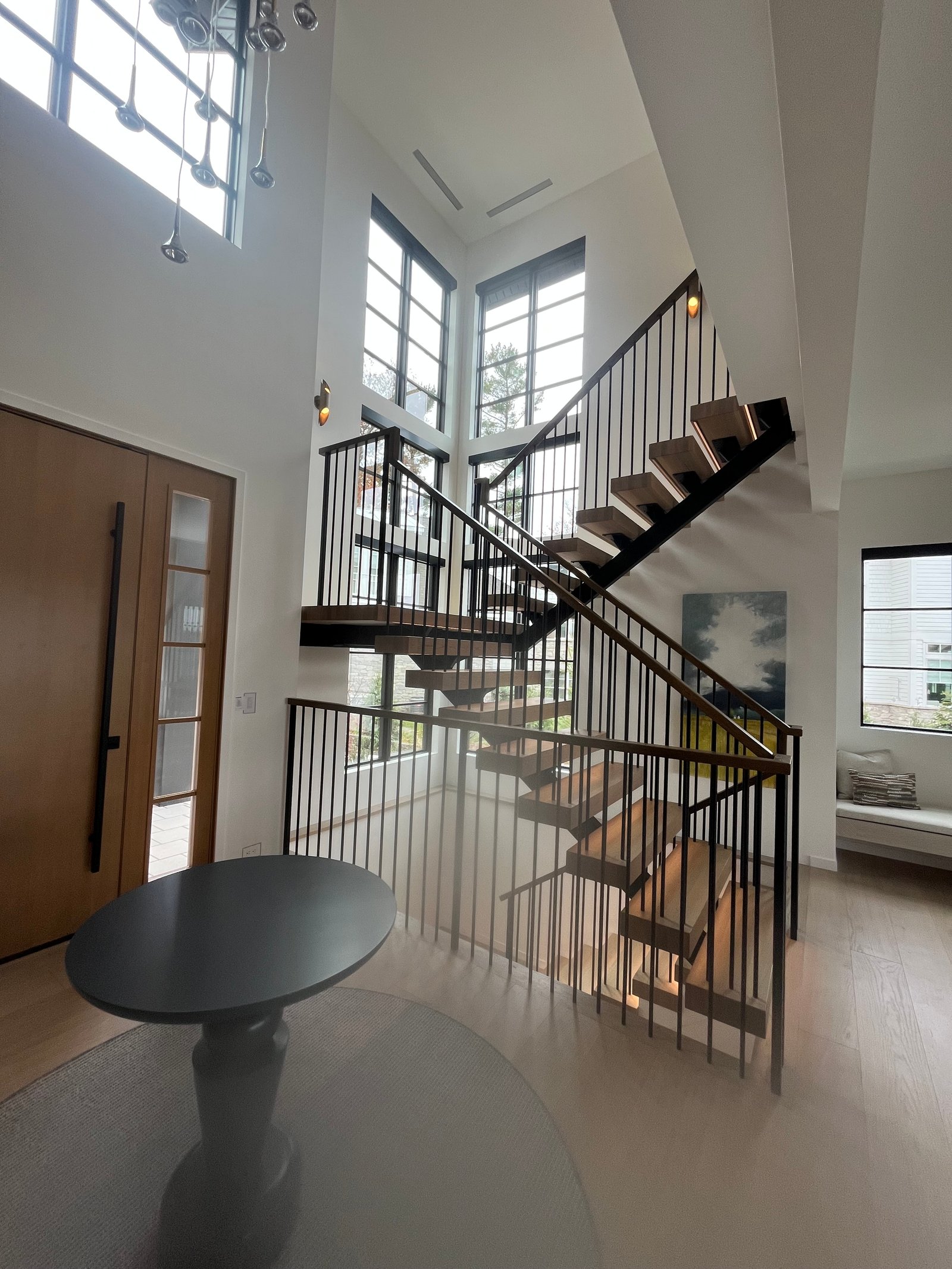 Modern multi-story interior with floating staircase, black metal railings, and bright windows